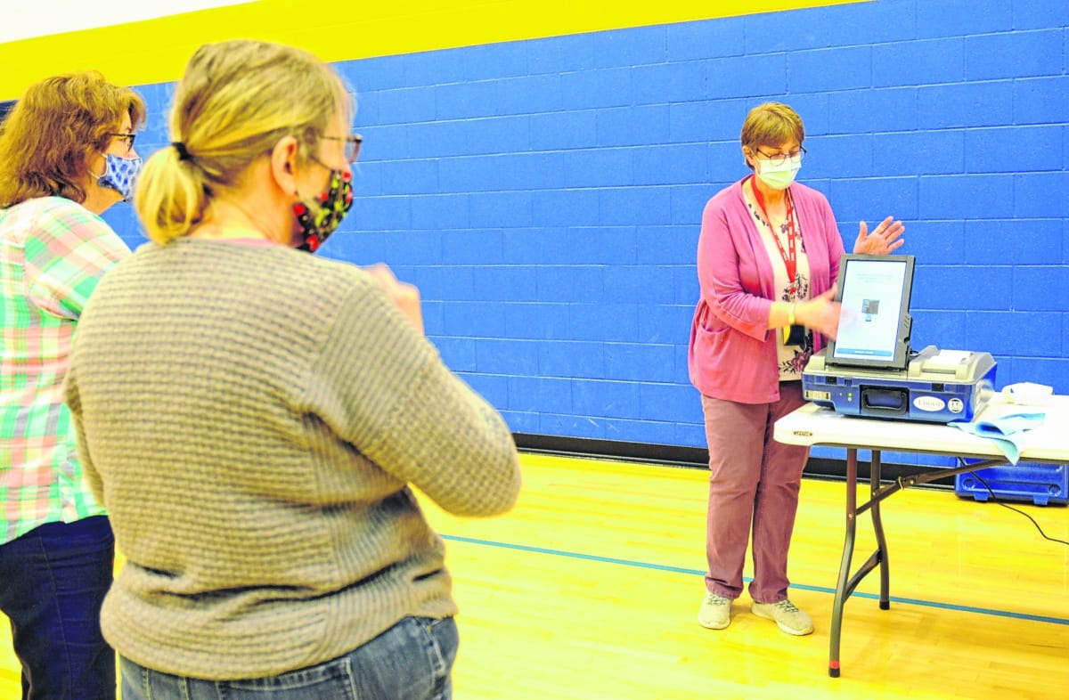 Poll workers watch Kathy Smith explain how the touch-screen voting machines work. Voters will be able to use these machines or old-fashioned pen-on-paper ballots when they go to vote in person this year.