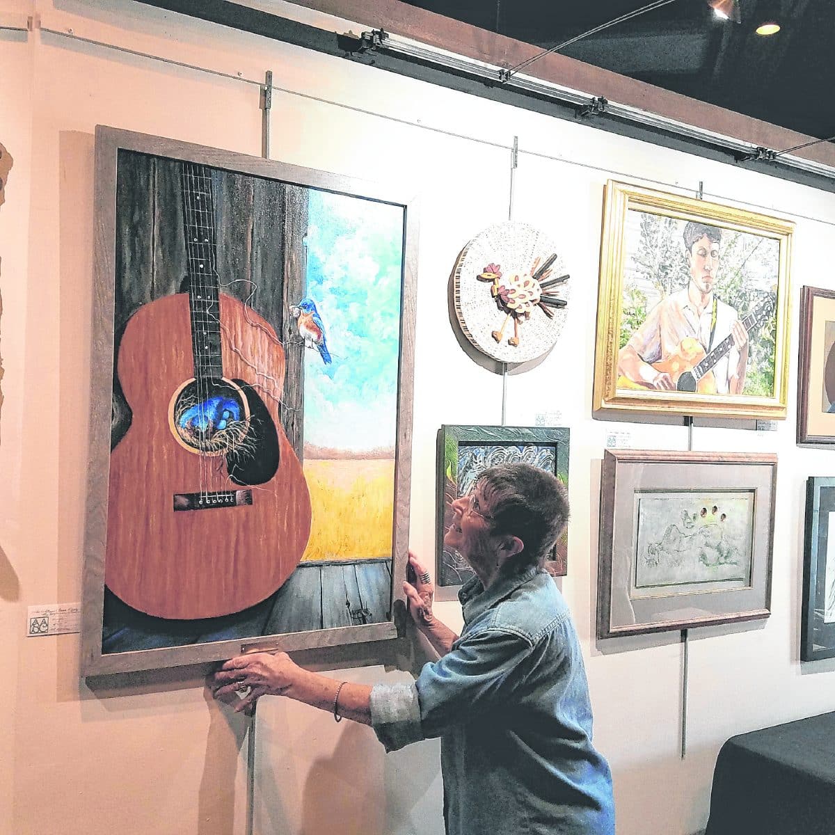 M.K. Watkins hangs artwork in the Brown County Playhouse gallery during the fingerstyle guitar competition. The show will hang through the middle of October. Submitted photo